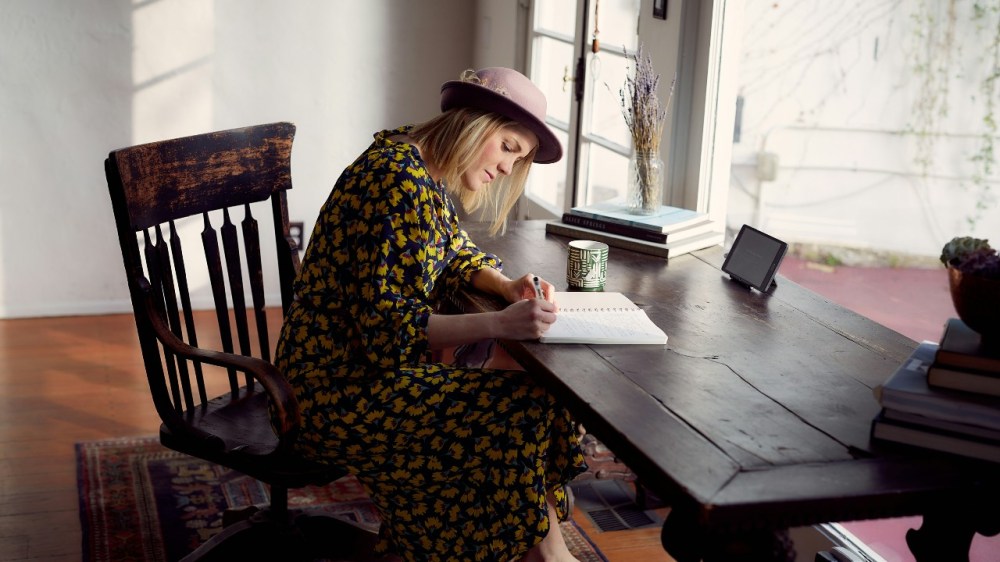 Woman sat at a large table, writing in a journal